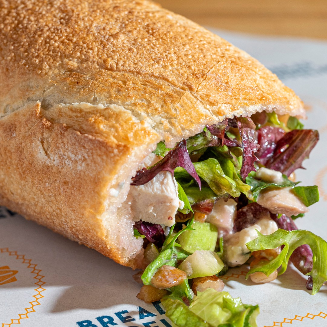 Close-up of a Bread Zeppelin chopped salad sandwich filled with fresh greens, chicken, and toppings inside a toasted baguette.