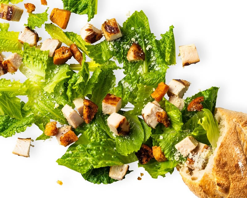 Fresh chopped salad with grilled chicken, crunchy croutons, romaine lettuce, grated cheese, and bread on the side, isolated on a white background.